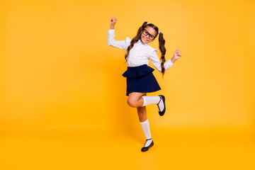 I'm happy because I'm going back to school! Full length, legs, body, size portrait of small girl isolated on bright yellow background stands on one leg raised her hands up