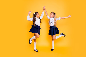 Fototapeta na wymiar Back to school concept. Full length, legs, body, size portrait of beautiful, charming, gorgeous, adorable, good-looking small girls hold hands looking at each other isolated on yellow background