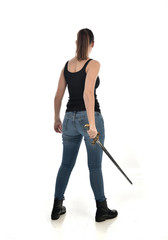 full length portrait of brunette girl wearing black single and jeans. standing pose holding a sword. isolated on white studio background.