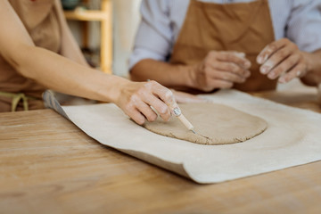 Working tool. Female ceramist wearing nice brown apron holding working tool while forming vase