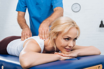 partial view of massage therapist doing massage to smiling woman on massage table in clinic