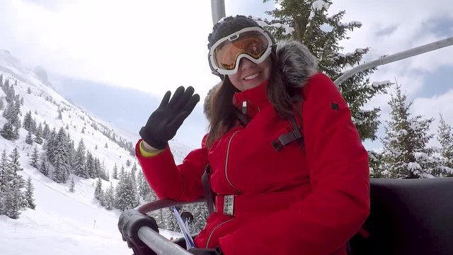 Woman Skier Climbs On The Chair Lift To The Top Of The Mountain And Waving Hand