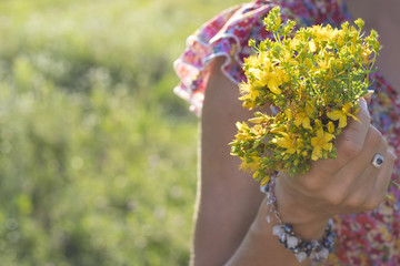 The girl is holding a small yellow bouquet of wild flowers.