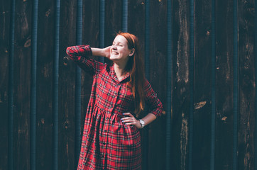 Fototapeta premium Smiling girl with long red hair standing in front of wood wall