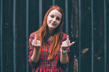 Red haired woman show middle fingers, fuck you off sign in front of a wood wall.