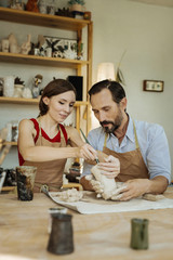 Making clay pot. Bearded dark-haired man feeling useful while helping his wife in making clay pot