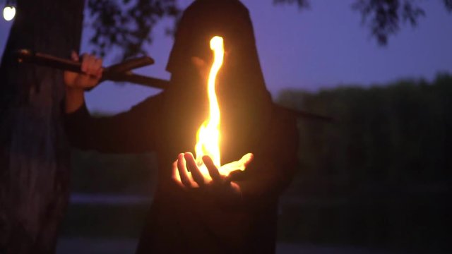 mysterious witcher in a cloak holding a fire man in fantasy medieval dress. Halloween