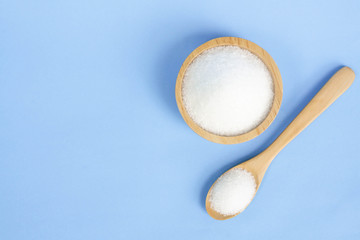 Top view monosodium glutamate in wood bowl and spoon on light blue background, food ingredient