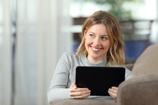 Woman thinking holding a tablet at home