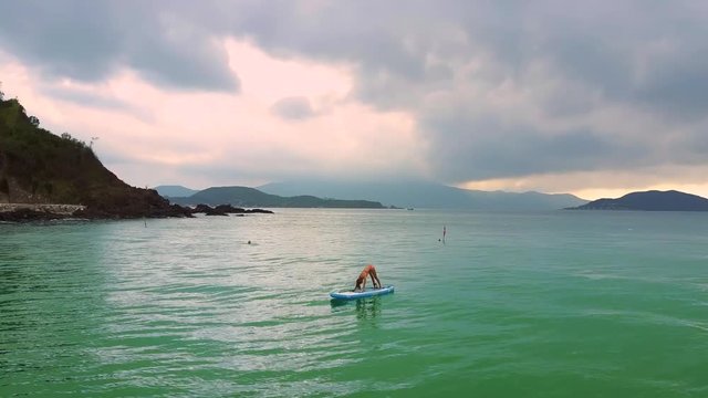 girl with ponytail stands in pose on paddleboard in ocean