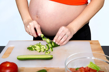 Young pregnant woman in the kitchen cooking vegetable salad, close-up. Healthy nutrition and pregnancy concept.