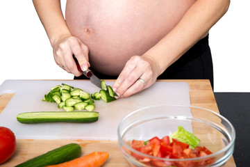 Obraz na płótnie Canvas Young pregnant woman in the kitchen cooking vegetable salad, close-up. Healthy nutrition and pregnancy concept.