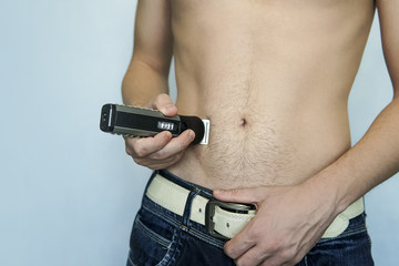 closeup of a young man trimming the hair of his pubis with an electric trimmer. concept of a clean healthy body for men. Man haircut pubic hair with a clipper. - obrazy, fototapety, plakaty