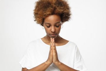 Closeup of young african american woman isolated on gray background putting hands together as if she is praying with closed eyes to overcome depression - Powered by Adobe