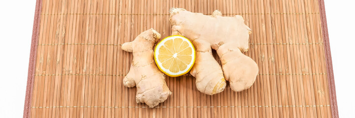 Two pieces of ginger and half a fresh lemon on a bamboo mat. View from above.