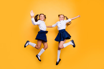 Dynamic images. 1-september concept. Full length, legs, body, size portrait of careless, cheerful, small girls in dark blue skirt, white blouse and black shoes jumping isolated on yellow background - obrazy, fototapety, plakaty