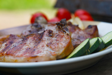 Portion of a grilled juicy pork chops with fresh tomato and cucumber salad