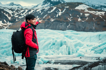 Fototapeta na wymiar Asian young man in red jacket looking the glacier in iceland