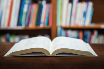 Education learning concept with opening book or textbook in old library, stack piles of literature text academic archive on reading desk and aisle of bookshelves in school study class room background