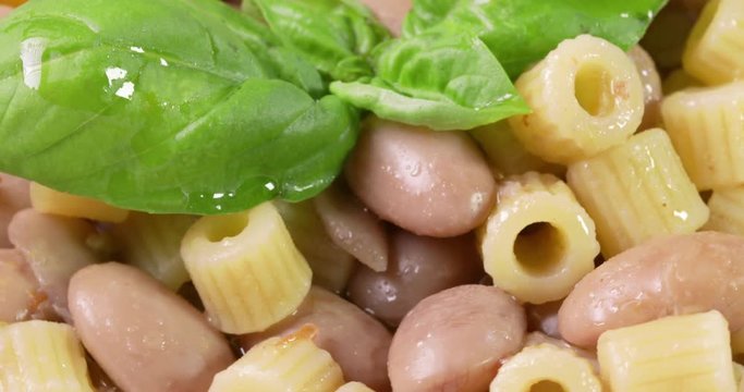 Italiana Pasta ditalini rigati e fagioli con foglie di basilico fresco e olio extra vergine di oliva su un piatto bianco isolato. Dieta Mediterranea. Vista macro.