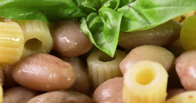 Italiana Pasta ditalini rigati e fagioli con foglie di basilico fresco e olio extra vergine di oliva su un piatto bianco isolato. Dieta Mediterranea. Vista macro.