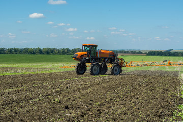 self-propelled sprayer works on a field under a blue sky with clouds