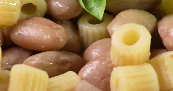 Italiana Pasta ditalini rigati e fagioli con foglie di basilico fresco e olio extra vergine di oliva su un piatto bianco isolato. Dieta Mediterranea.