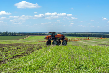 Fototapeta premium self-propelled sprayer works on a field under a blue sky with clouds