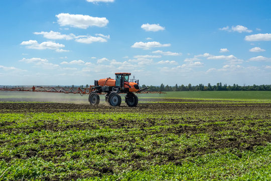 self-propelled sprayer works on a field under a blue sky with clouds