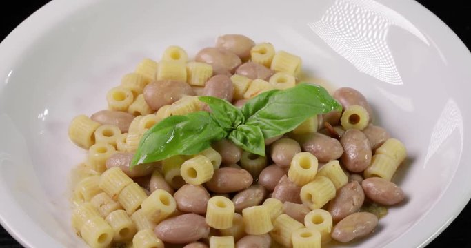 Italiana Pasta ditalini rigati e fagioli con foglie di basilico fresco e olio extra vergine di oliva su un piatto bianco isolato. Dieta Mediterranea.