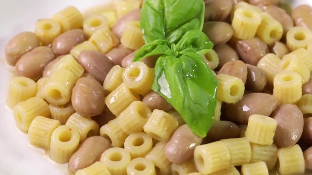 Italiana Pasta ditalini rigati e fagioli con foglie di basilico fresco e olio extra vergine di oliva su un piatto bianco isolato. Dieta Mediterranea.