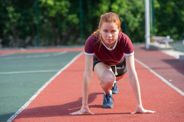 Obraz premium the red-haired student in shorts gives the standards for running for a short distance at the physical education class at an open sports ground.Female athlete ready to run on running track