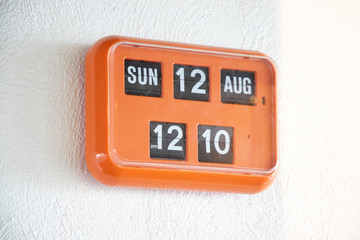 orange flip clock on white wall, retro analog timer. show time on 12 august at lunch time.