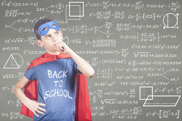 Back to school concept with super hero school kid thinking hard in front of a blackboard