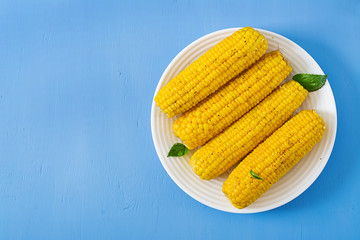 Boiled corn in white plate on blue background. Summer food. Top view. Flat lay