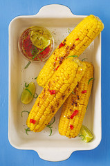 Grilled sweet corn with mexican sauce, chilli and lime on blue background. Healthy summer food. Top view. Flat lay