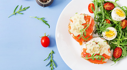 Tasty breakfast. Open sandwiches with salmon, cream cheese and rye bread in a white plate and salad with tomato, egg and arugula. Top view. Flat lay