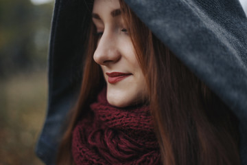 Close up portrait of beauty european young woman with full lips. The girl turned her head to the right. Woman wearing in grey coat with hood and in red scarf. 