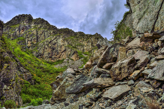 Picturesque cloudy summer landscape of mountain gorge in the Altai Mountains, Russia. Cracked limestone rocks covered with moss and lichen and a pile of huge boulders in  foreground
