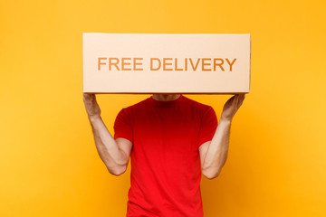 Man in red uniform isolated on yellow orange background. Professional male employee courier or dealer in t-shirt holding empty cardboard box Free delivery. Receiving package service concept Copy space