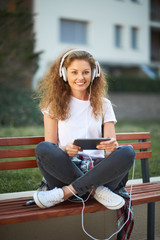 Young woman sitting on bench with legs crossed and listening to the music.