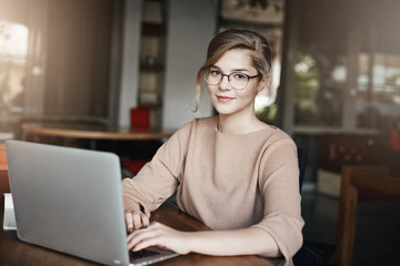 Creative and attractive female graphic designer working under project while sitting in cafe with...