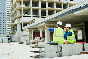 Back view portrait of two workers wearing hardhats  communicating while enjoying coffee break on...