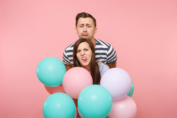 Fototapeta na wymiar Portrait of young fun crazy mad couple in love. Woman and man in blue clothes celebrating birthday holiday party on pastel pink background with colorful air balloons. People sincere emotions concept.