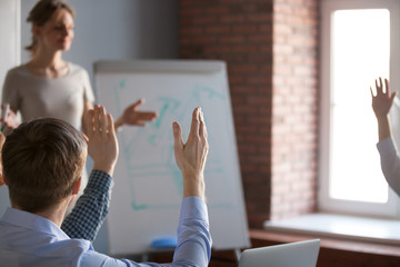 Workers raising hands asking questions during training or educational seminar in office, people answering coach, brainstorming at team meeting during businesswoman speaker presentation. Close up view
