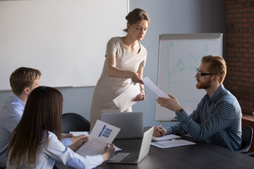 Millennial businesswoman give handout materials to work team members during flipchart presentation, female speaker or coach share documents to workers, presenter hand papers to consider or analyze