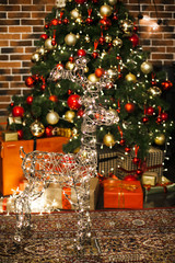 Beautiful Christmas deer with the glowing lights at night in living room with decorated Christmas tree, gifts. New Year loft interior with New year tree with red and gold decor balls
