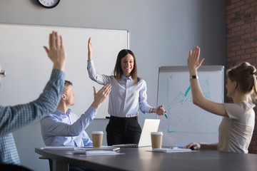 Smiling young businesswoman giving corporate training for diverse work group, employees raising...