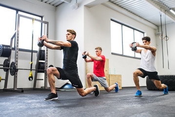 Three young men in gym doing exercise with kettlebells.