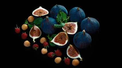 Fresh blue figs on black background. Beautiful violet figs with with red and yellow raspberry berries. copy space. close up